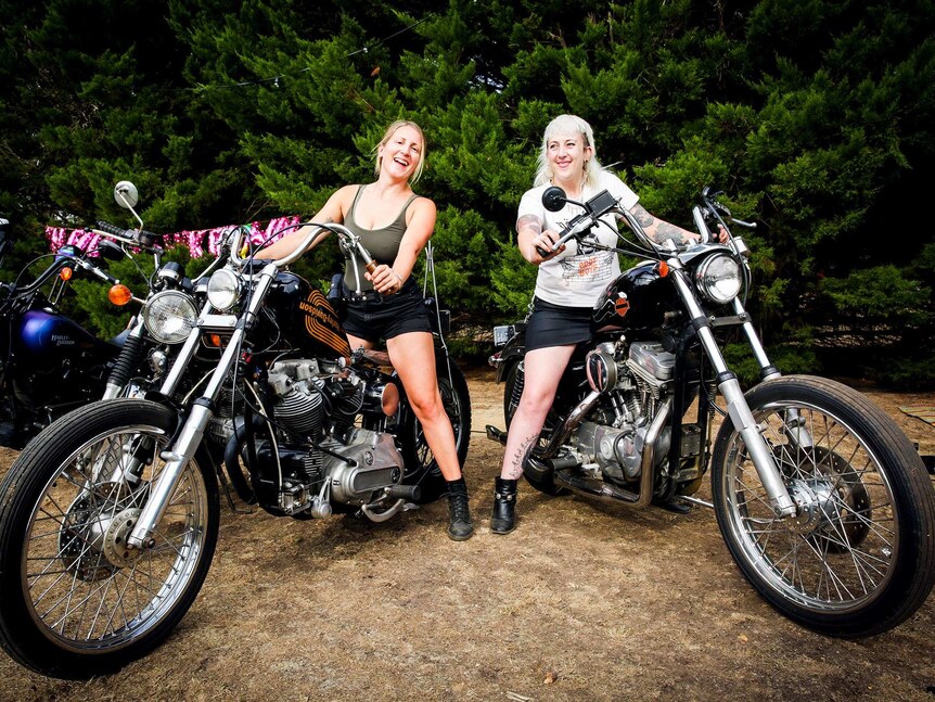 A blonde woman in a singlet and a tattooed woman with bleached hair on their bikes
