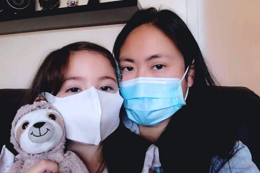 A woman and a girl both wear face masks as they pose for a photograph taken inside a home.