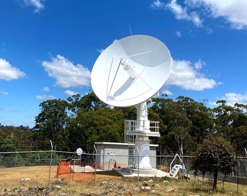 A white telescope dish points towards a blue sky