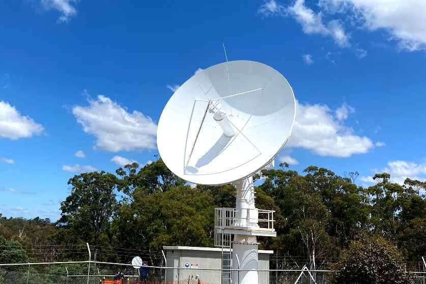 A white telescope dish points towards a blue sky
