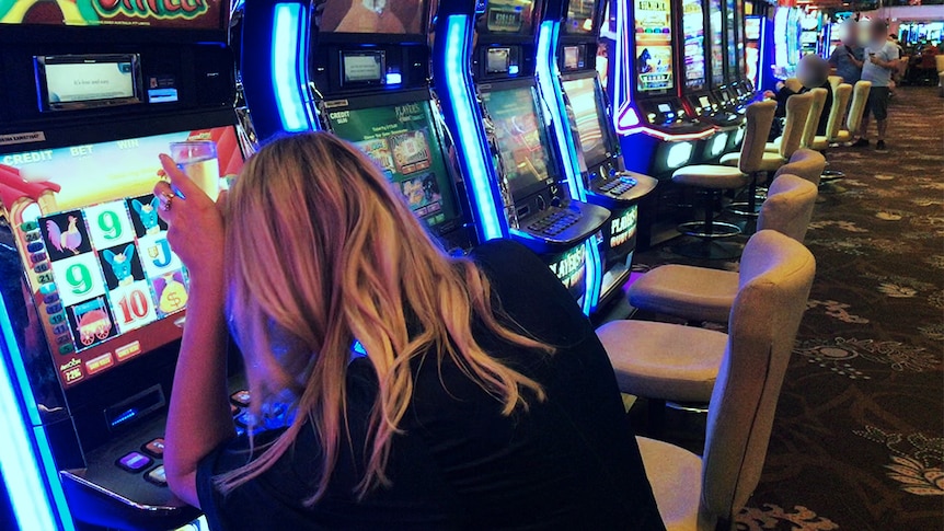 A blond woman sits with a drink at a pokie.