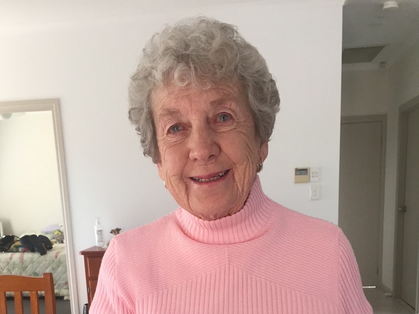 An elderly woman wearing a pink jumper while reading a book