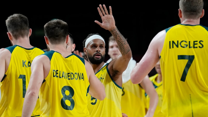 Australia basketball captain Patty Mills raises his hand as teammates walk around him.