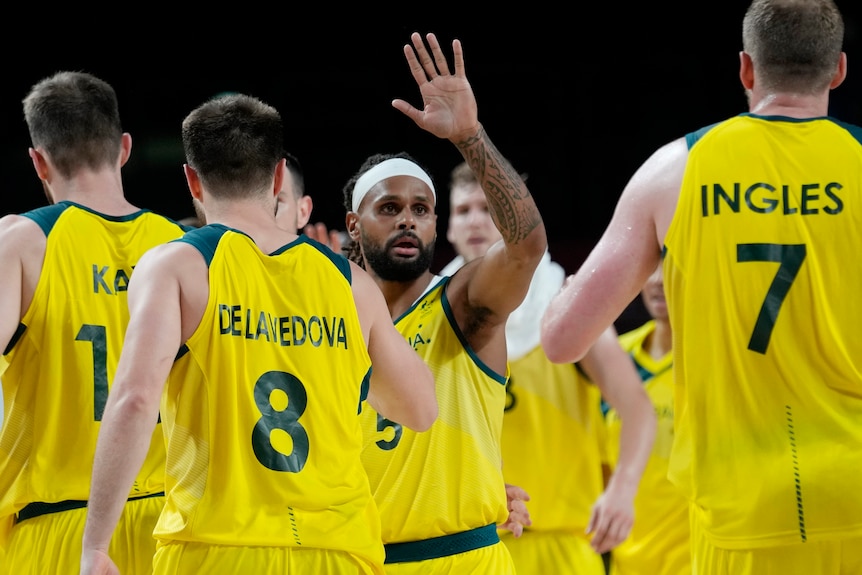 Australia basketball captain Patty Mills raises his hand as teammates walk around him.