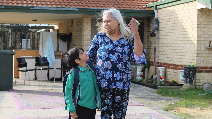 Ms Williams looks down at her grandson, who is looking up at her. They stand in front of her house.