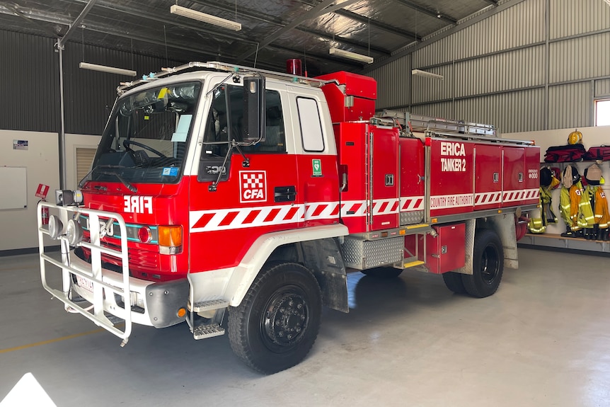 Erica's red CFA fire truck, named 'Tanker 2' sits in the garage with CFA volunteer uniforms hanging up on the wall behind it.