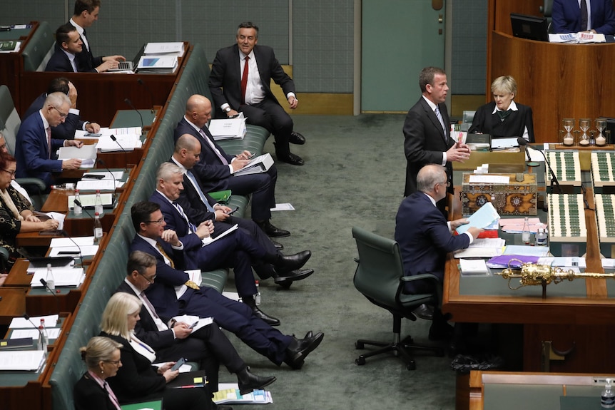 Mostly male MPs sitting in the house of representatives, wearing suits and ties and on their phones behind the prime minister