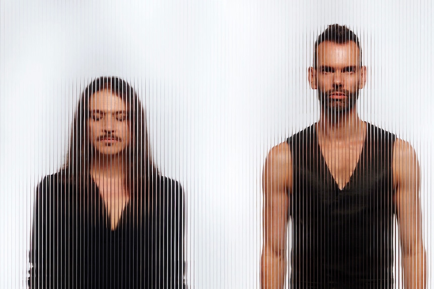 Brian Molko and Stefan Olsdal of Placebo behind textured glass. Molko has eyes closed, Oldsal wears a v-neck singlet