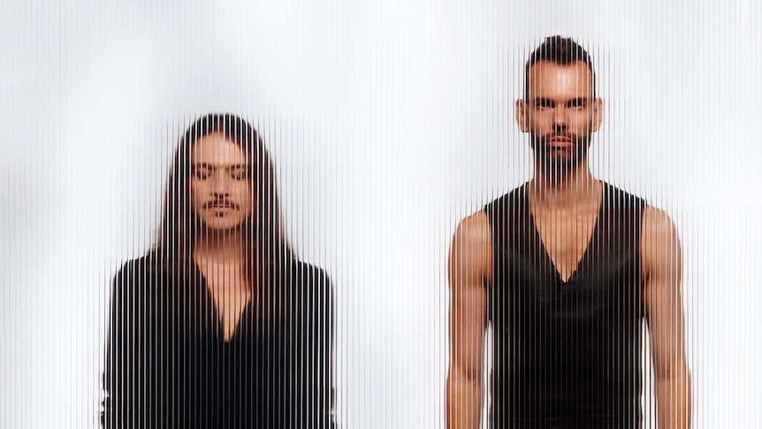 Brian Molko and Stefan Olsdal of Placebo behind textured glass. Molko has eyes closed, Oldsal wears a v-neck singlet