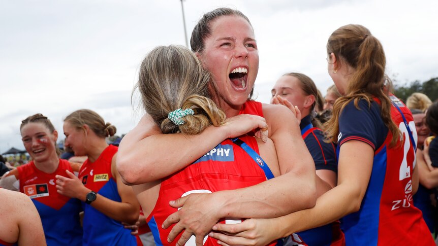 Kate Hore hugs Melbourne Demons teammates and shouts after winning the AFL Women's grand final.
