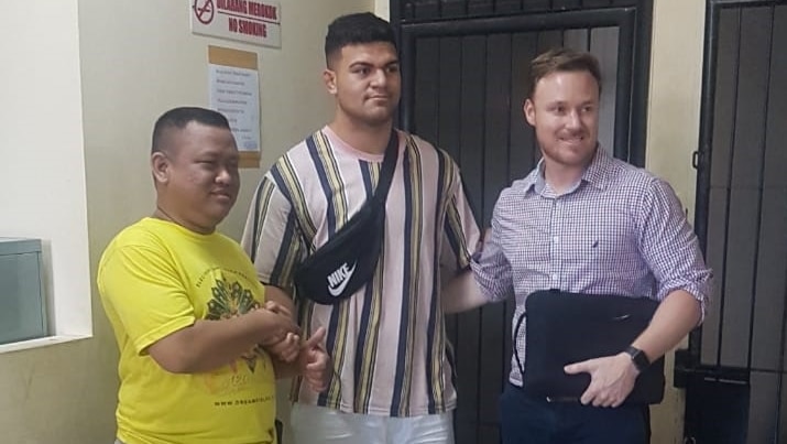 David Fifita, centre, poses for a photo with a man on his left and another on his right outside what appears to be a cell.