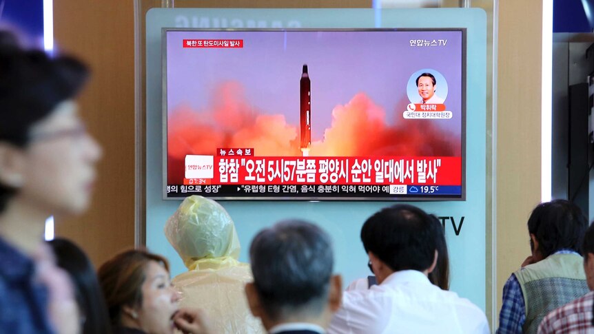 A missile launch is seen on a TV screen as a crowd of people watches in a train station.