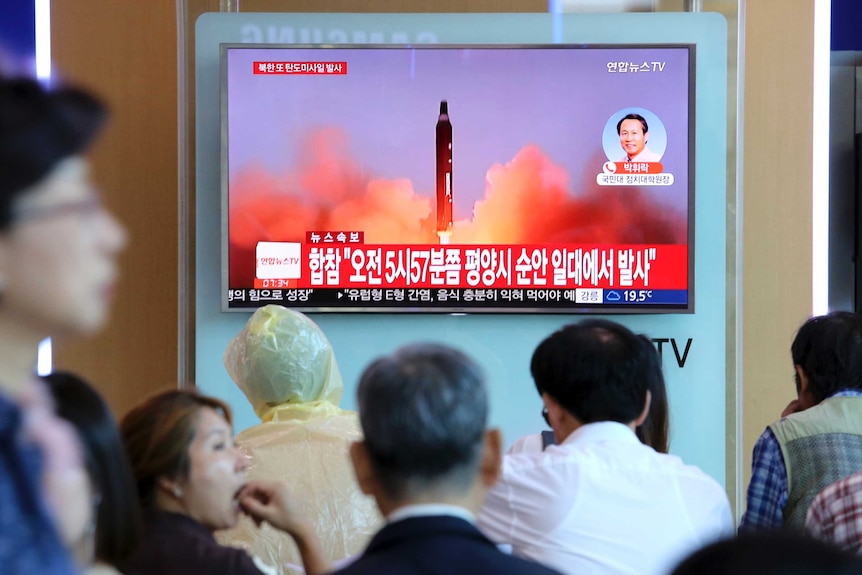 A missile launch is seen on a TV screen as a crowd of people watches in a train station.