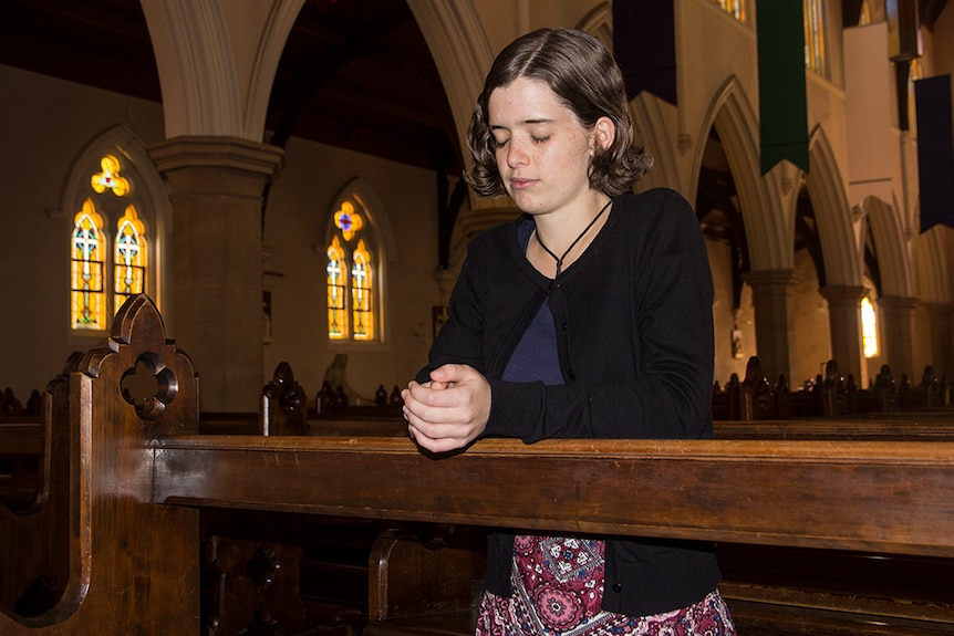 Nancy Webb kneels at a pew praying in a cathedral.