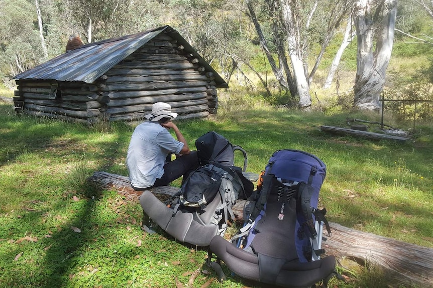 Man sits on a log beside a log cabin