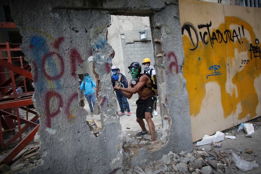 A masked anti-government demonstrator breaks down a wall to release pieces of concrete to throw at police during a protest.