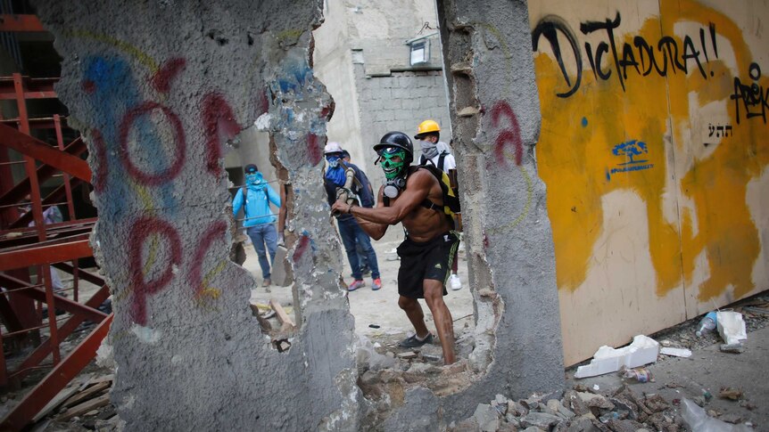 A masked anti-government demonstrator breaks down a wall to release pieces of concrete to throw at police during a protest.