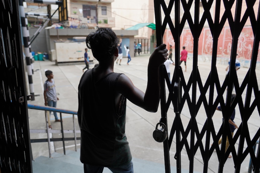 An Indian boy leans on a gate as he watches children playing in a courtyard 