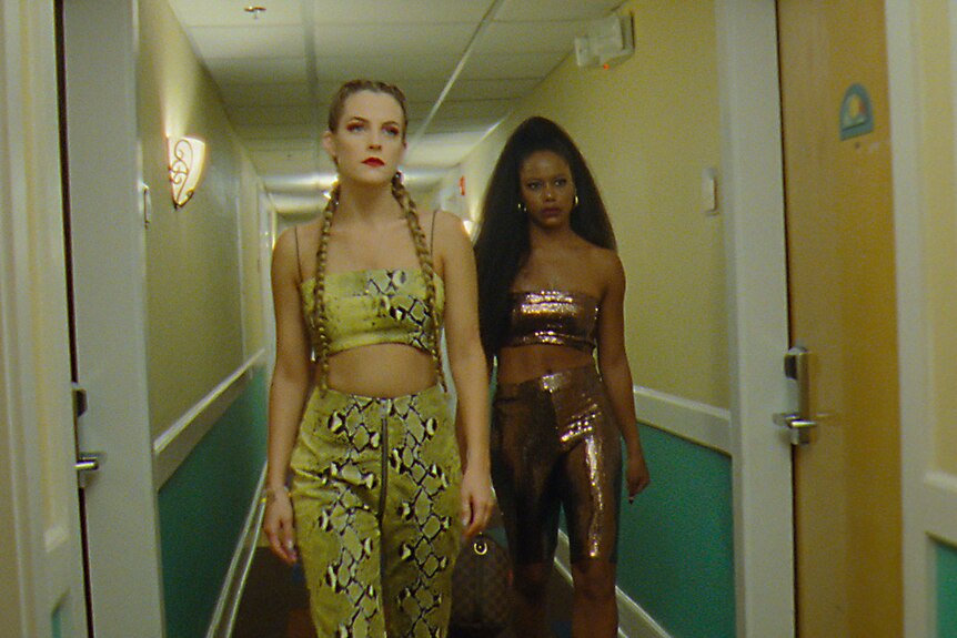 White woman wears matching yellow animal print crop and pants in hallway with black woman wearing brown glitter crop and pants.