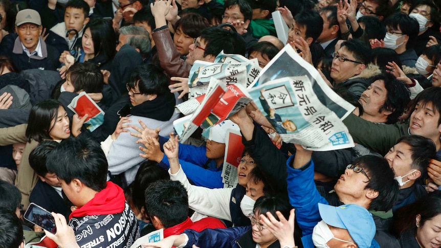 From above you see lots of people crushed up against each other trying to grab newspapers.