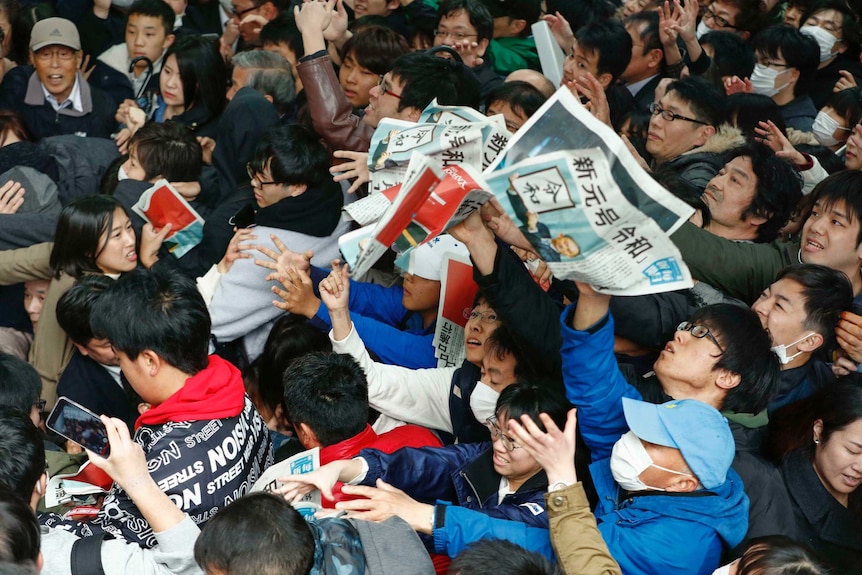 From above you see lots of people crushed up against each other trying to grab newspapers.