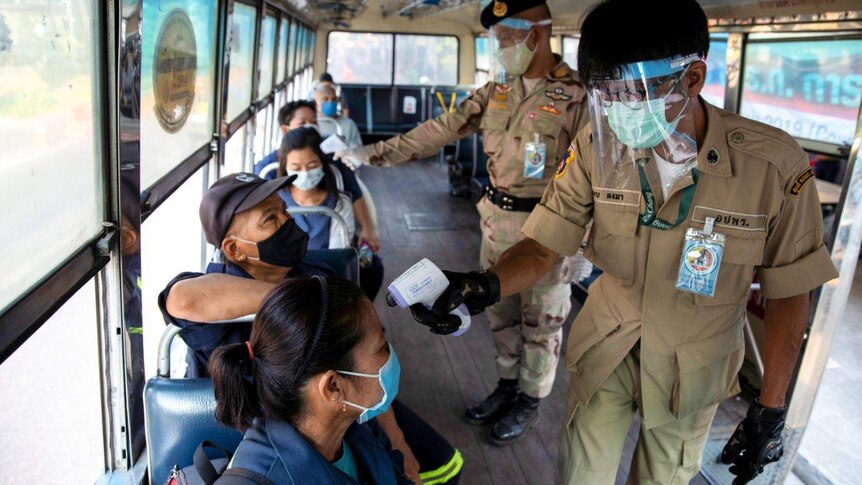 Two Thai officers taking temperatures on buses