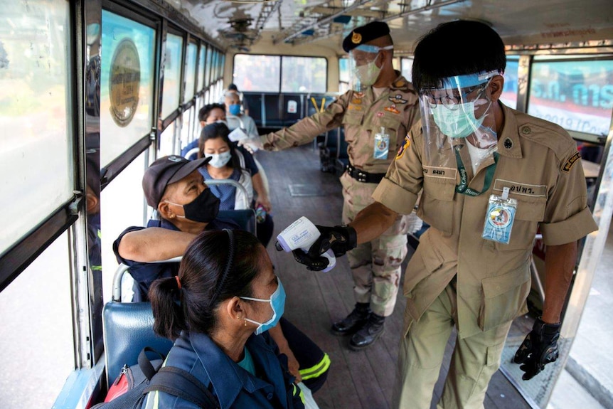 Two Thai officers taking temperatures on buses