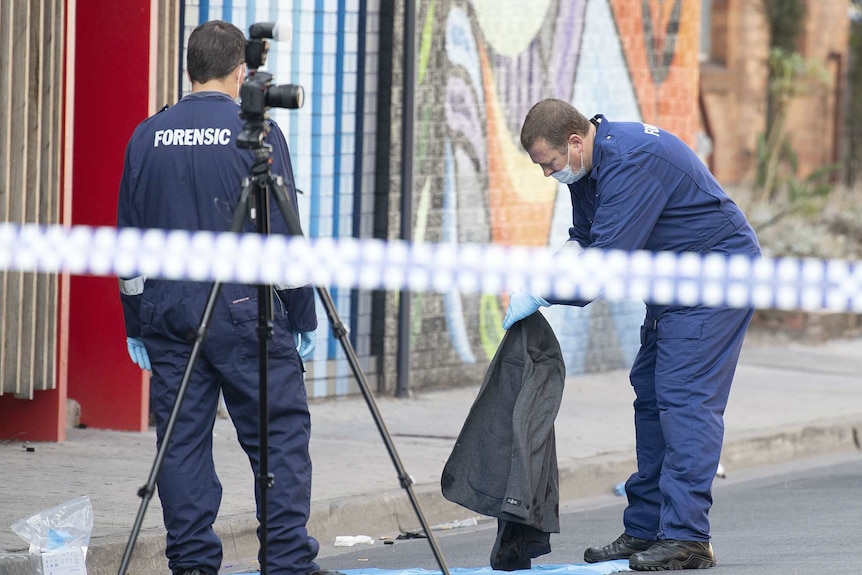 Forensic police examine items including a grey jacket at the Prahran crime scene which is marked off with police tape.