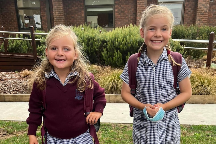 Two little girls in school uniforms grinning in front of school building