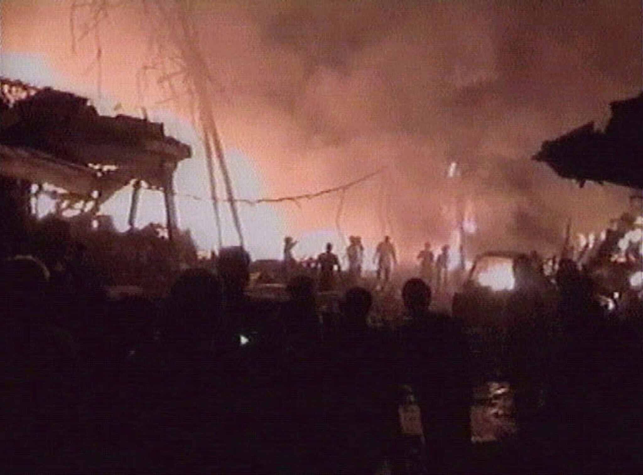 People are seen silhouetted as they watch fires blaze in the wreckage of buildings and cars following bomb blasts.