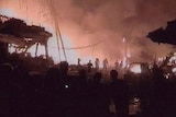 People are seen silhouetted as they watch fires blaze in the wreckage of buildings and cars following bomb blasts.