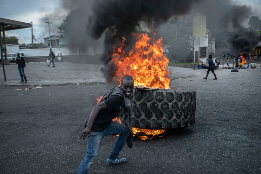 un homme jette un pneu sur une barricade en feu