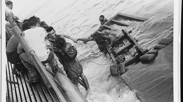 A black and white photo of prisoners of war being rescued from the water and helped onto a ship.