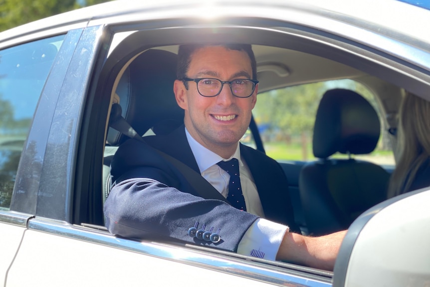 A man wearing a suit while sitting in the driver's seat of a car