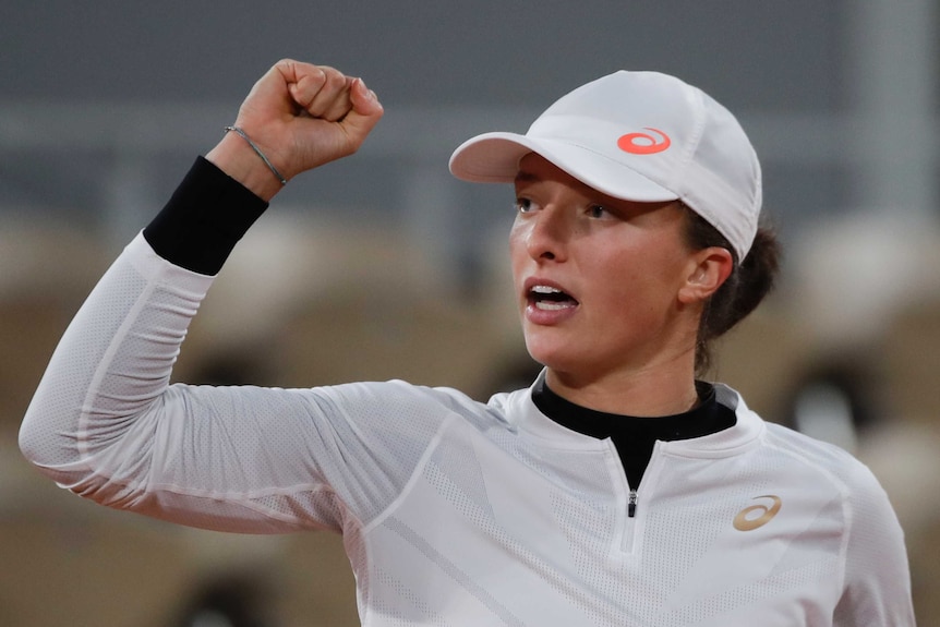 A cap-wearing tennis player looks to side of court and pumps her fist in celebration at French Open.