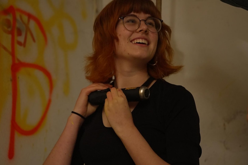 A young woman with red hair smiles as she holds a D-lock around her neck.