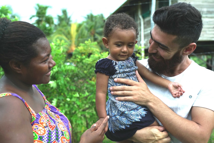 A father holds his toddler daughter while her mother looks on