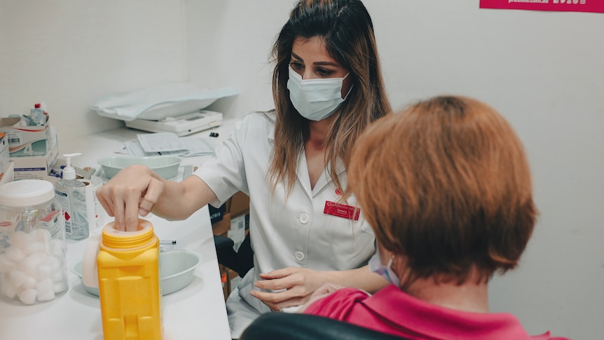 A pharmacist wearing a mask disposes of a needle after administering a COVID-19 vaccine to a patient.