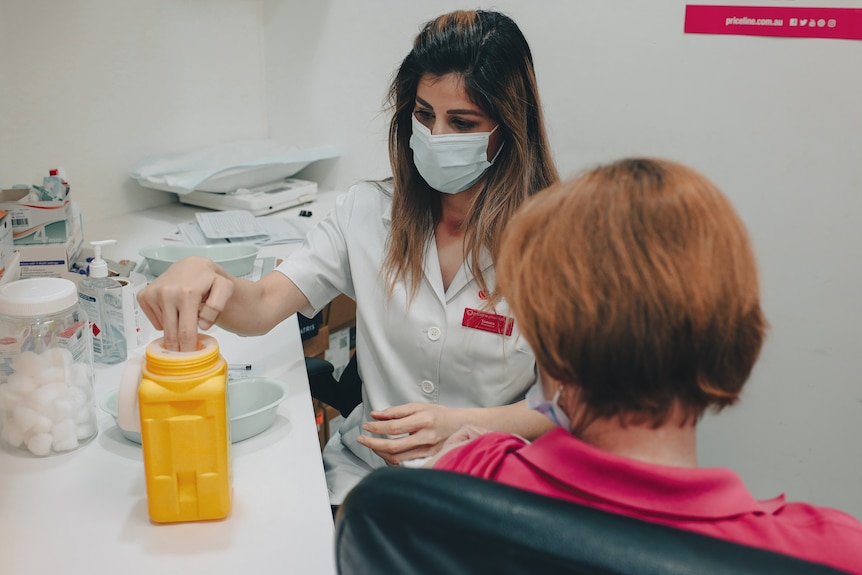 a masked pharmacist preparing a vaccine shot with a woman