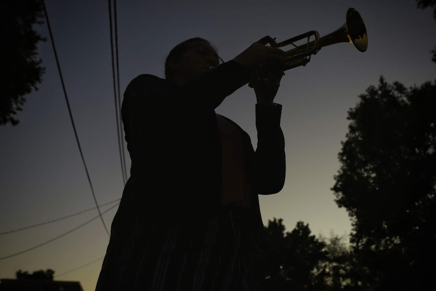 A woman in silhouette playing a trumpet at dawn