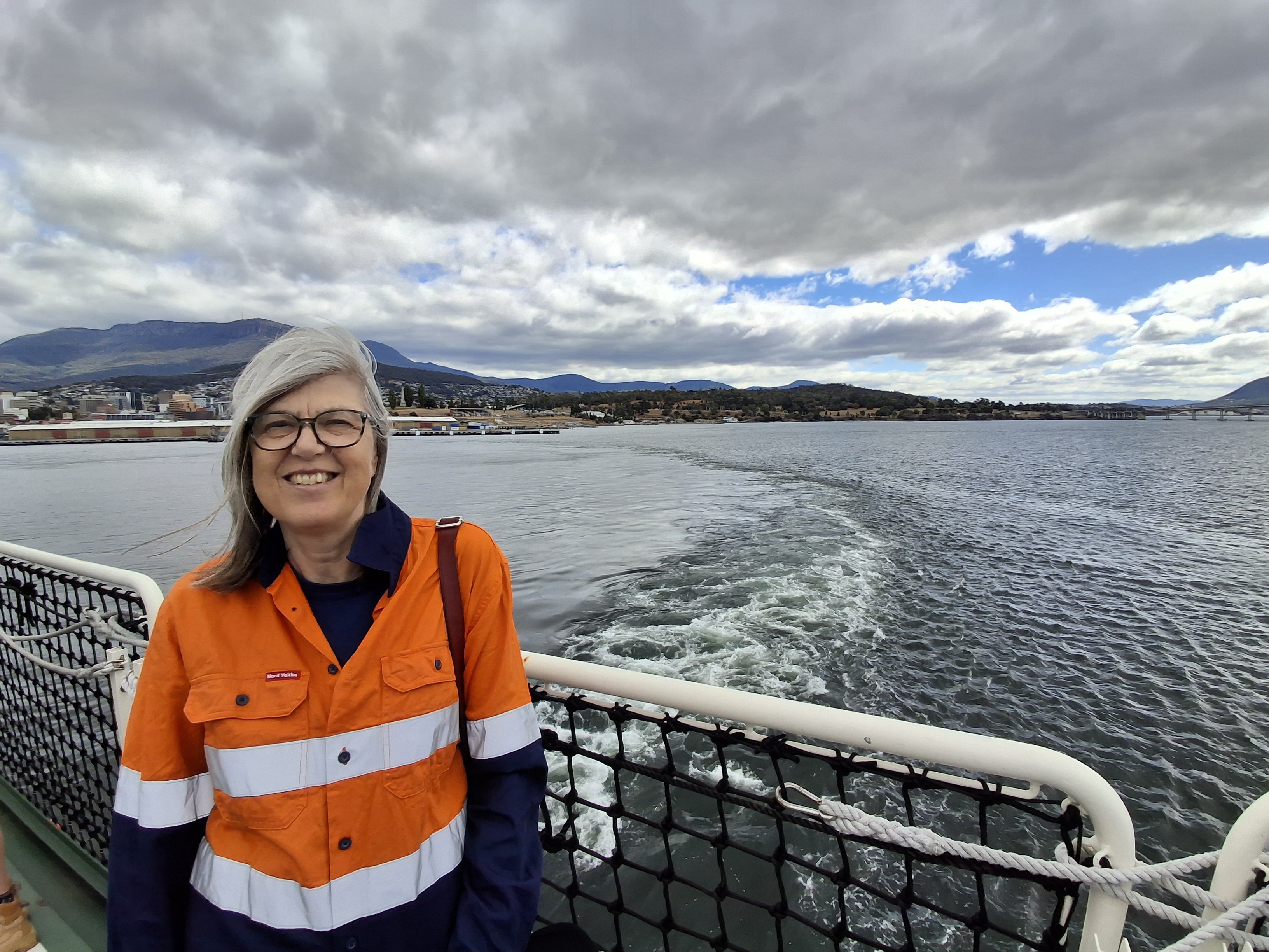 A middle aged woman with a work shirt on stands on board a vessel off the coast of Tasmania.