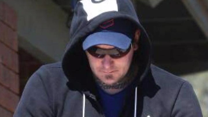 Karl Holt, wearing sunglasses and a hoodie, is led out of a building.