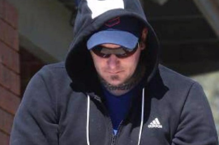 Karl Holt, wearing sunglasses and a hoodie, is led out of a building.