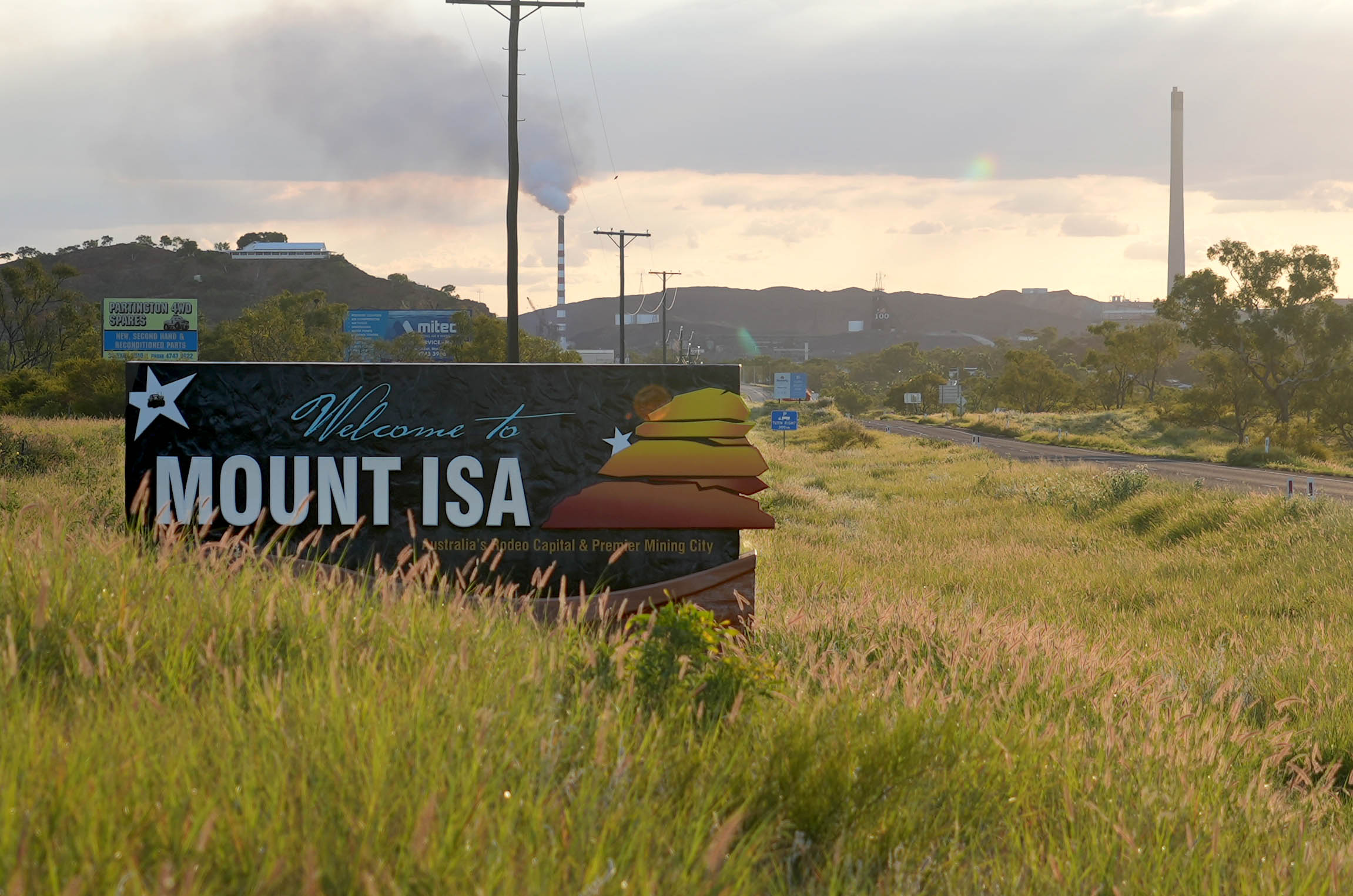 Tall grass around a sign reading Welcome to Mount Isa by the roadside. 