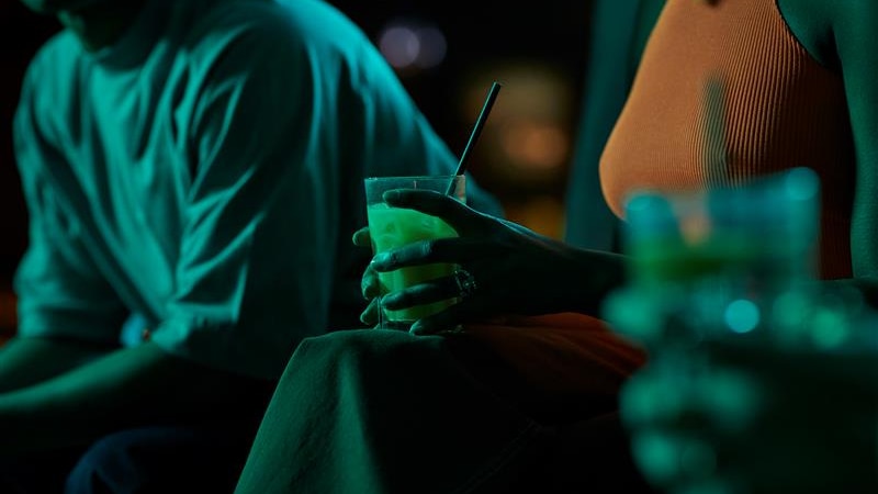 A lady is holding a drink in a dimly lit bar. 