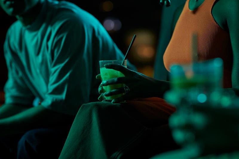 A lady is holding a drink in a dimly lit bar. 