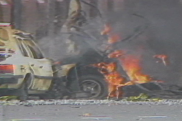 A grainy image of a wrecked car on fire.