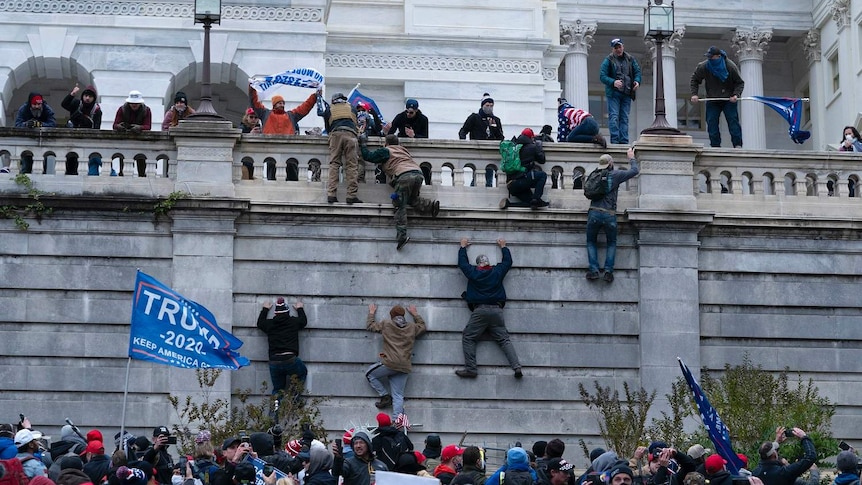 Trump supporters climb a stone wall during a riot at the US Capitol.