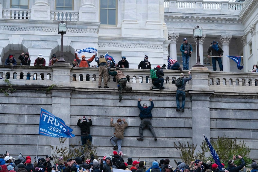 I sostenitori di Trump scalano un muro di pietra durante una rivolta al Campidoglio degli Stati Uniti.