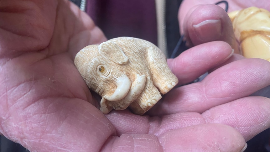 mammoth figurine with amber eyes in palm of man's hand